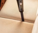 Person using a handheld vacuum to clean a beige sofa in Nakuru during the holidays