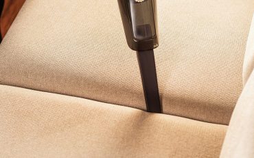 Person using a handheld vacuum to clean a beige sofa in Nakuru during the holidays